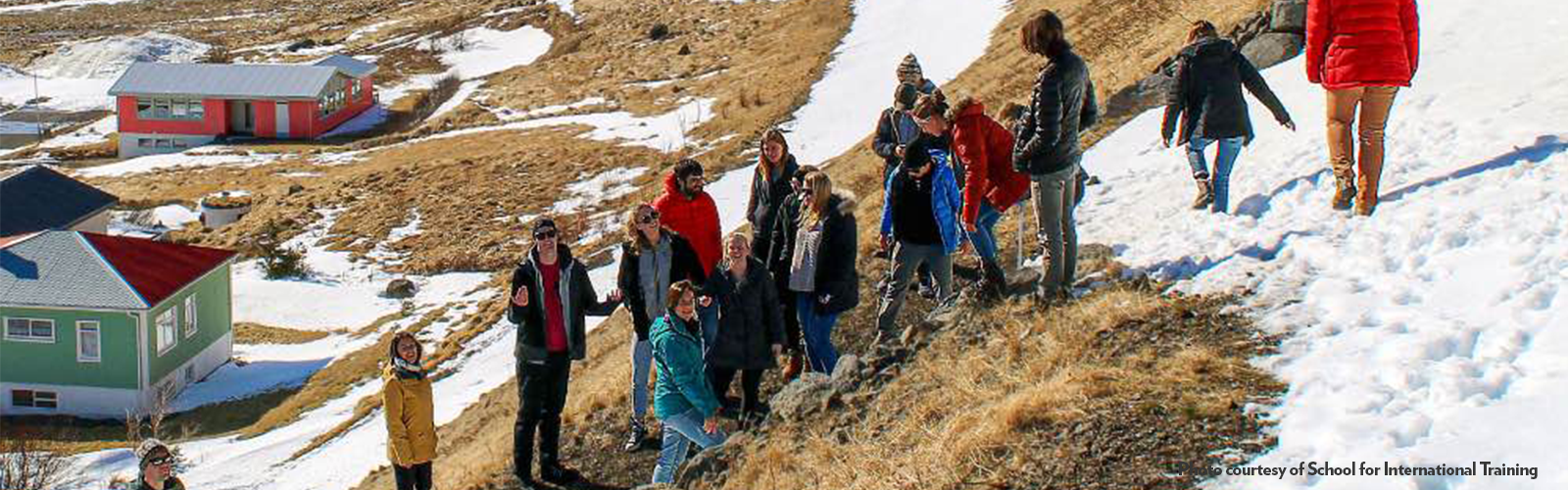 Fifteen students wearing warm clothes climb up a mountain covered in patchy snow. 